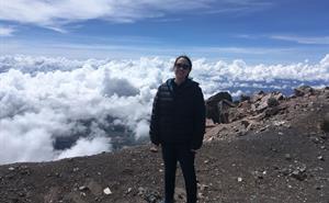 Eimear Gallagher is standing on a mountain top and she is above the clouds which can be seen in the background.
