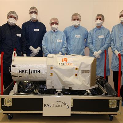 Engineers in cleanroom suits standing behind a large camera built for ISS.