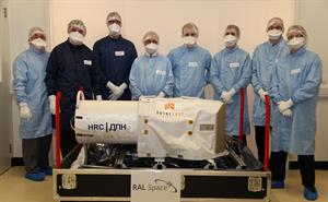 Engineers in cleanroom suits standing behind a large camera built for ISS.