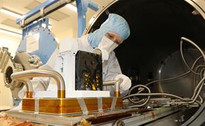 PITMS instrument being taken out of the thermal vacuum chamber by an engineer in a clean room suit.