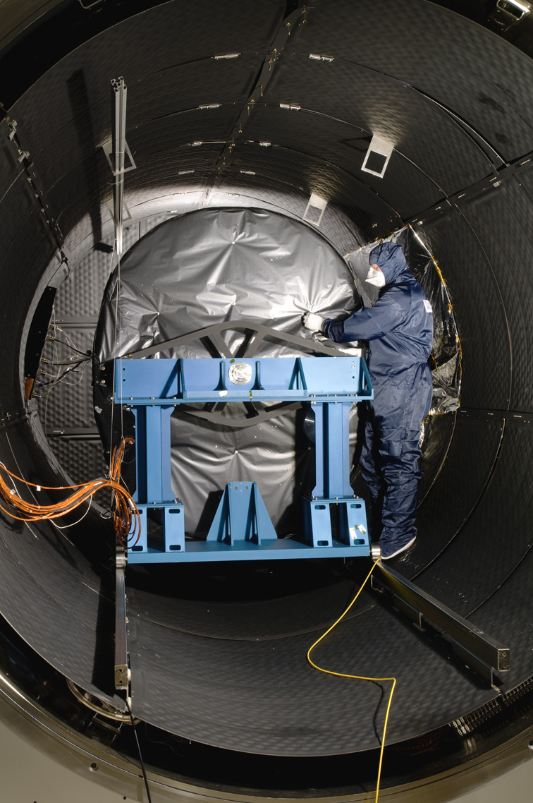 An engineer in a cleanroom suit securing the MIRI instrument in the thermal test chamber. MIRI is wrapped in a themal blanket.