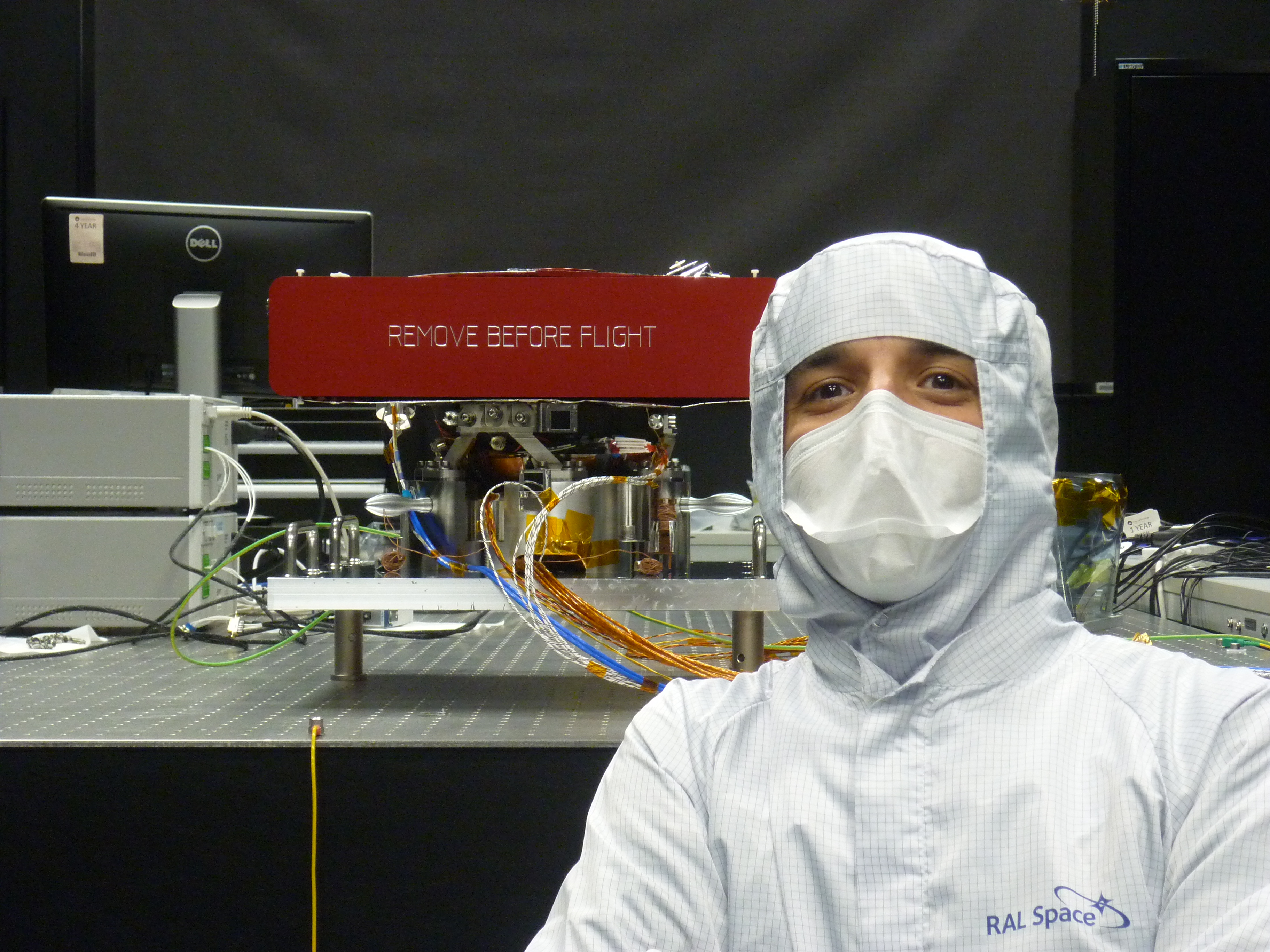 Man in a clean room suit stands in fron of the PCS.