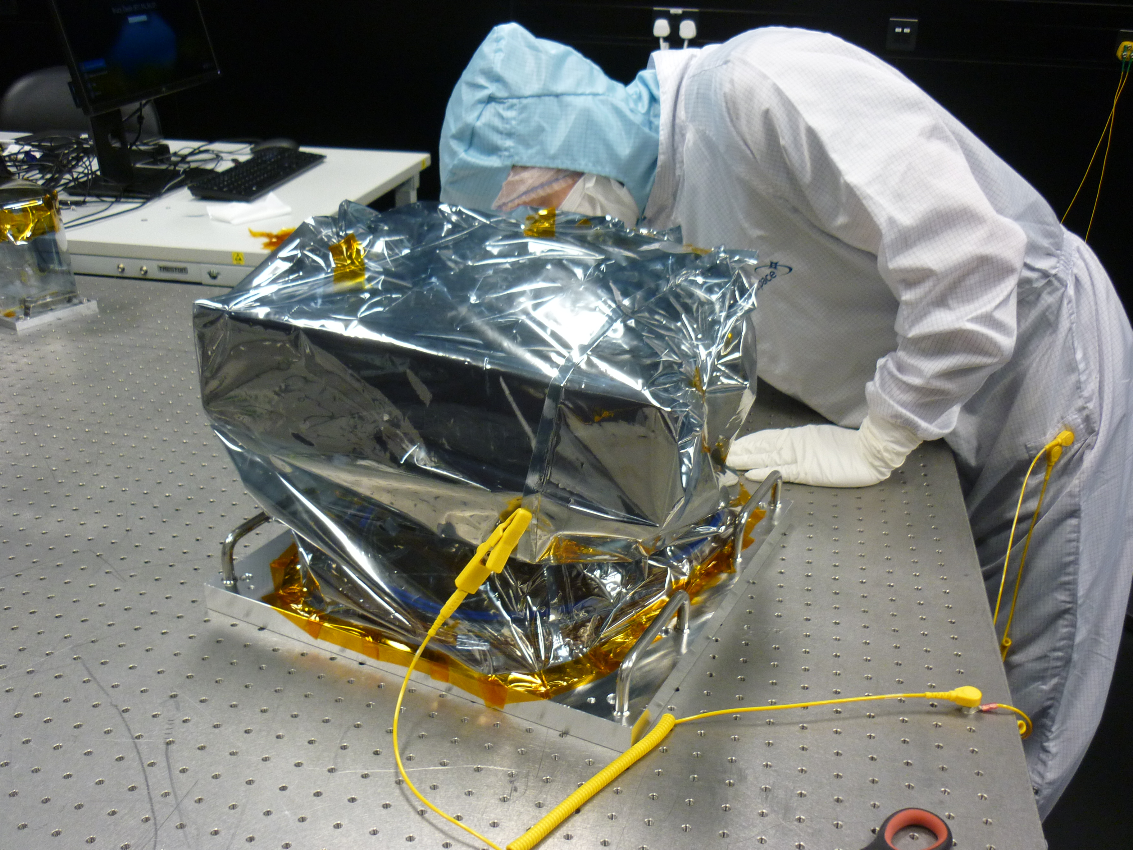 Technician in a clean room suit bends down behind the PCS.