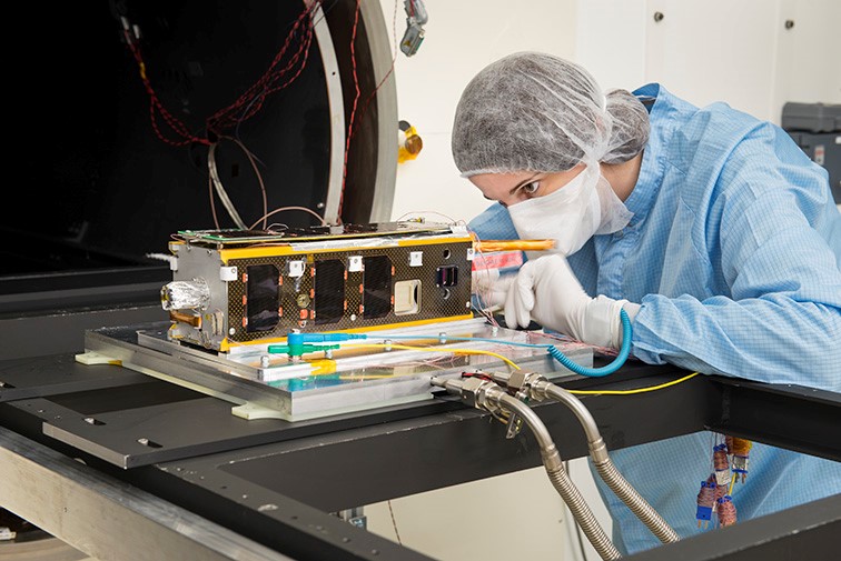 An engineer prepares a small sat for testing.