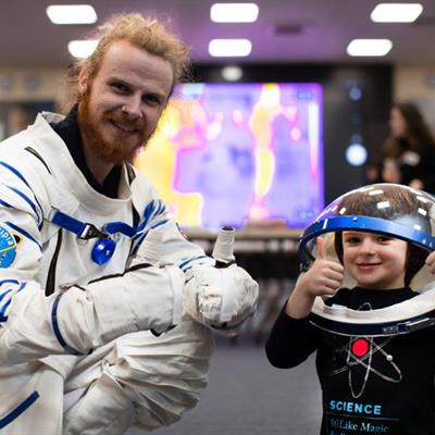 RAL Space engineer tries on astronaut suit, a child wears the helmet.