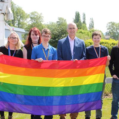 Group shot of the LGBTQ+ Group pictured at the Rutherford Appleton Laboratory. with the Pride rainbow flag.