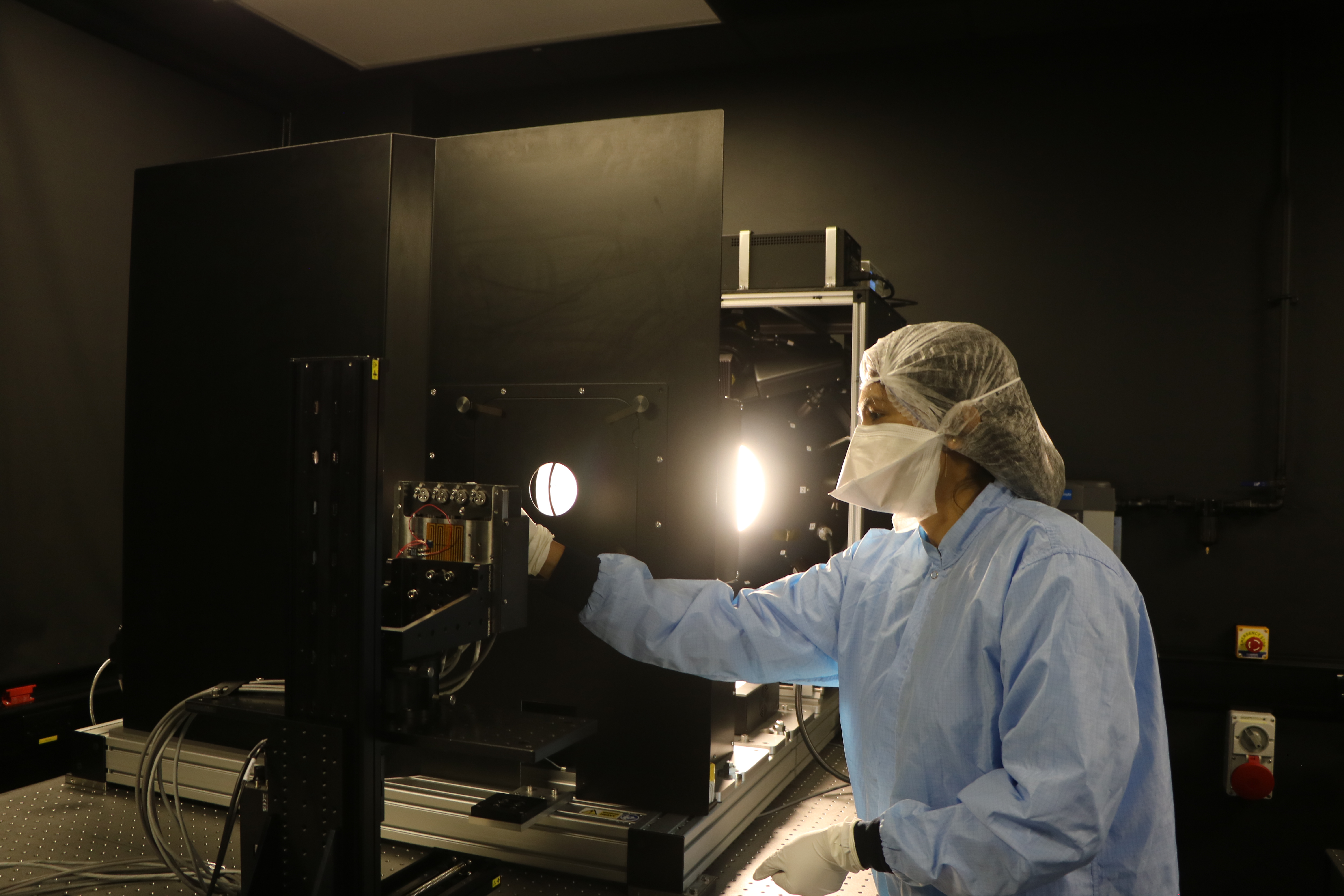 A person in a cleanroom gown and mask setting up equipment.