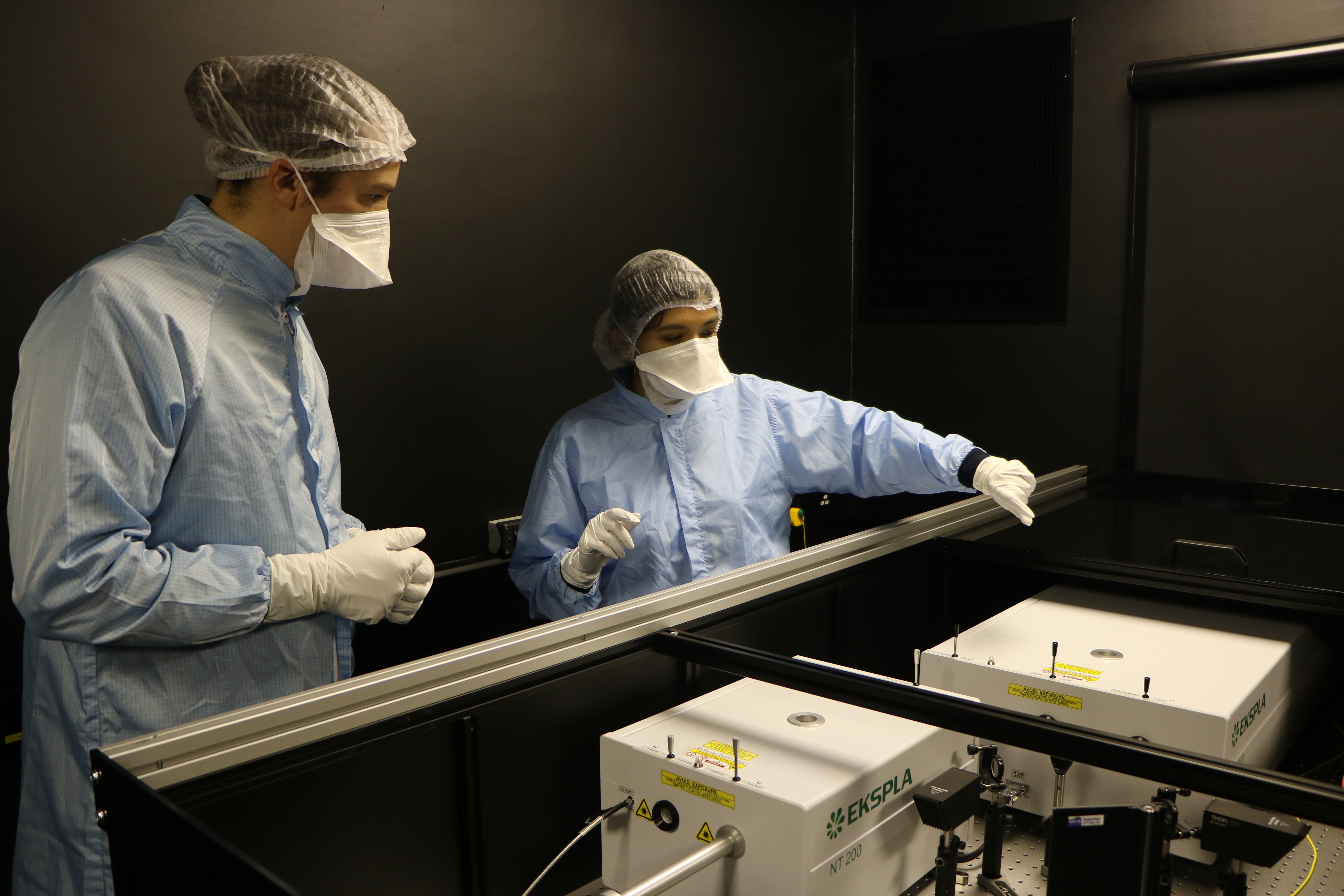 Two people in cleanroom gowns pointing at equipment