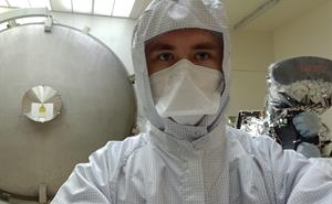 Ben Keeble wearing a clean room suit, standing outside of RAL Space's 3-metre space test chamber next to the SLSTR instrument.