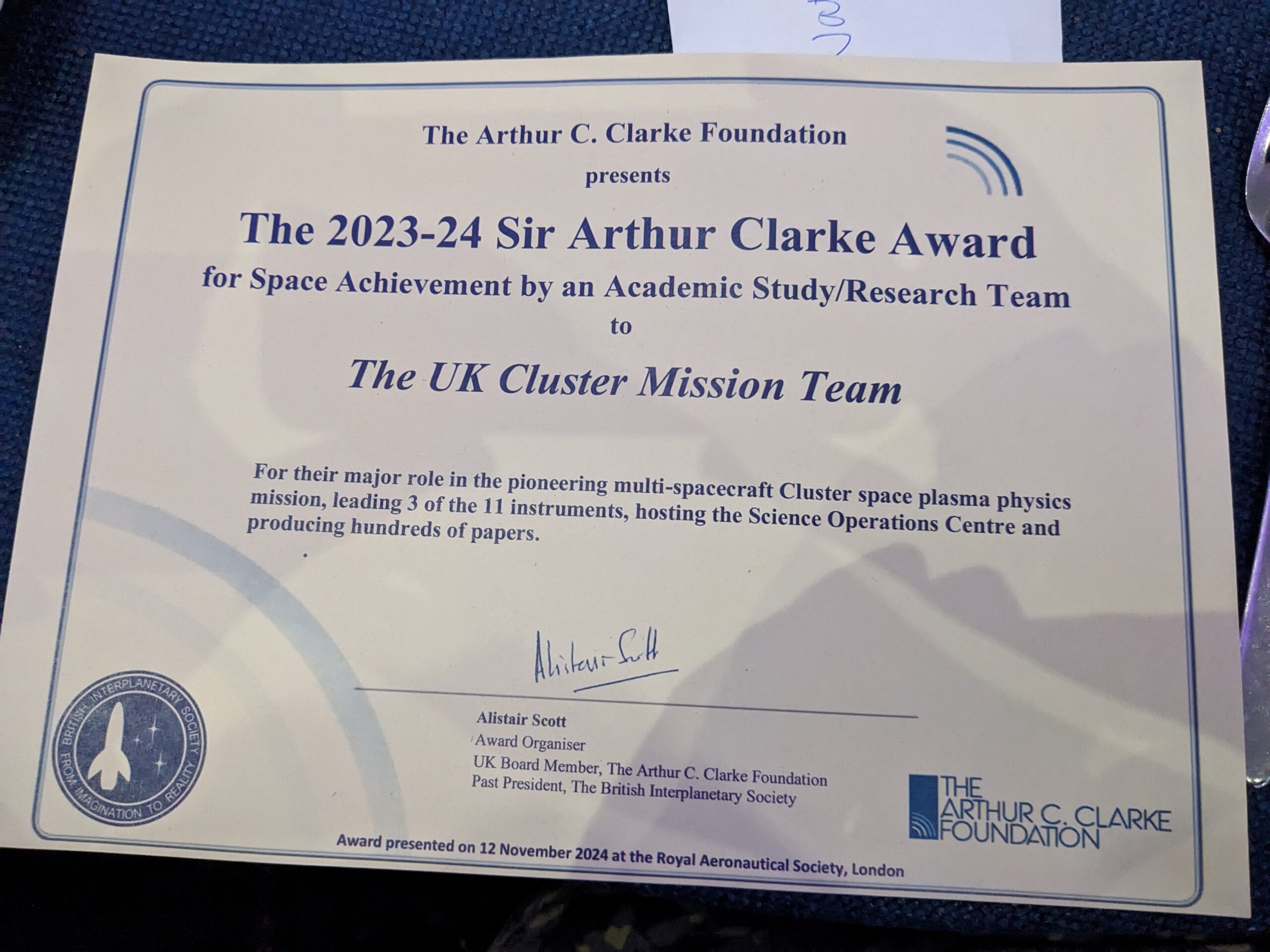 Photograph of the certificate presented alongside the Sir Arthur Clarke Award. It reads "To the UK Cluster Mission Team, for their major role in the pioneering multi-spacecraft Cluster space plasma physics mission, leading 3 of the 11 instruments, hosting the Science Operations Centre and producing hundreds of papers."