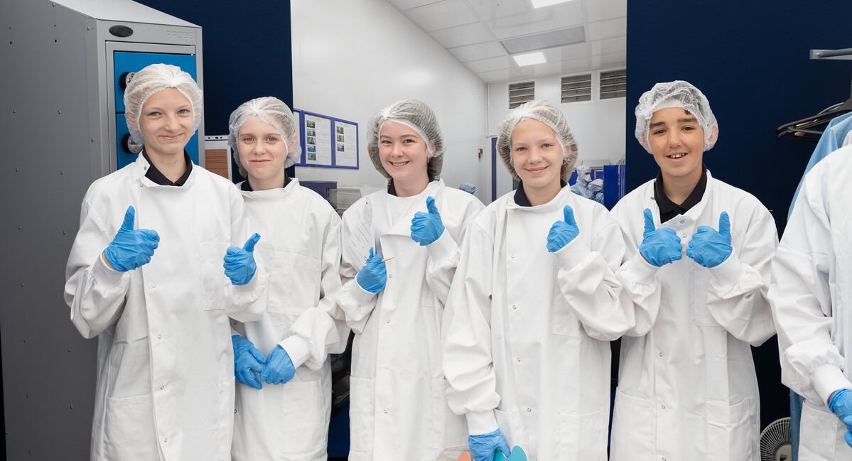 School students dressed up in clean room outfits, smiling with their thumbs up.