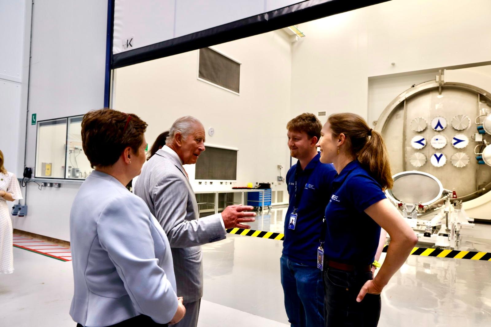 The King speaking to RAL Space staff in front of a clean room containing a space test chamber and the Ariel telescope's structural model.
